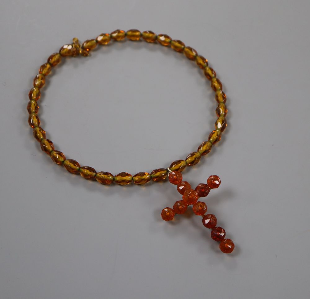 A gilt metal and facet cut amber set cross pendant, 6cm, on a similar amber necklace, gross weight 35 grams.